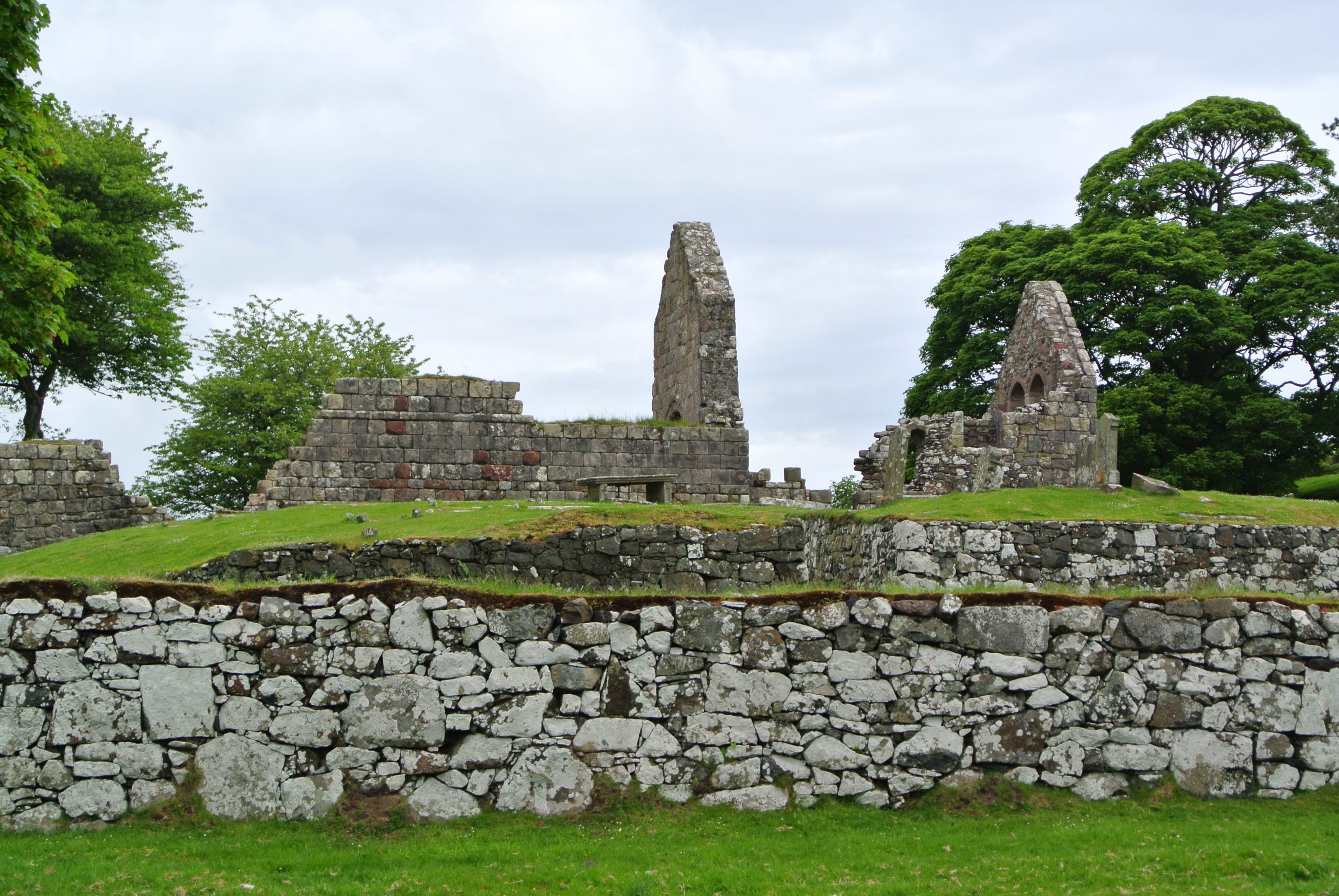 ruins of a stone built church, surrounded by a stone wall with green grass around it.